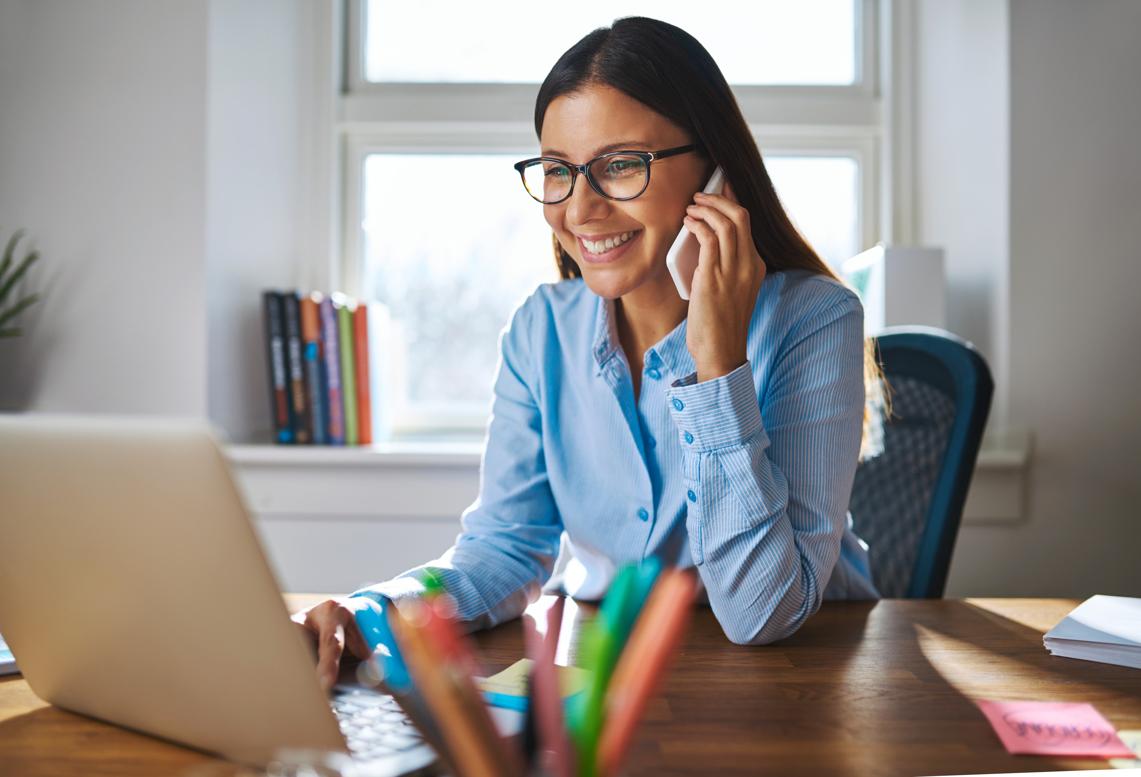 A smiling business owner working at her laptop while speaking on the phone.