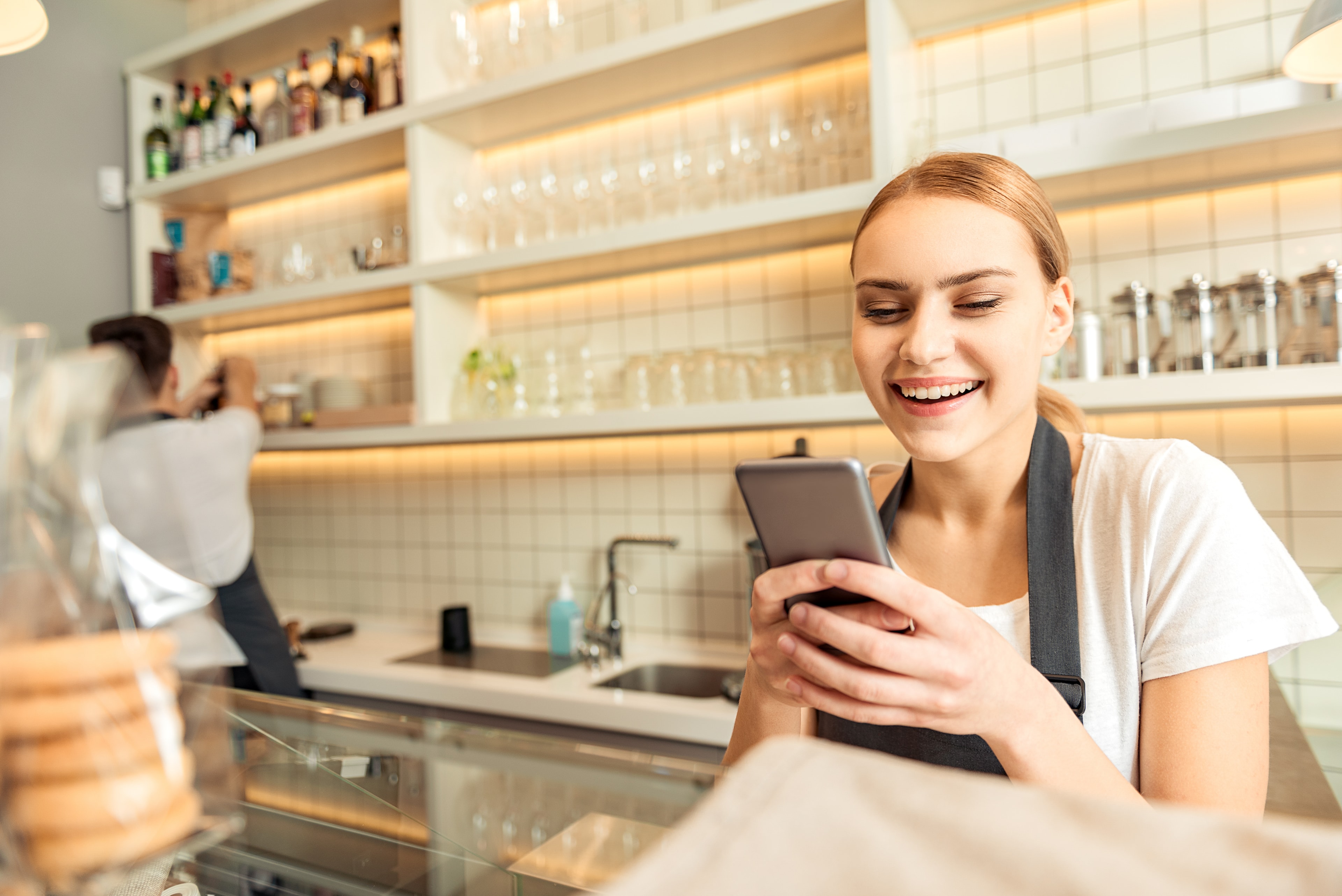 A café employee smiling as she uses her phone at work.