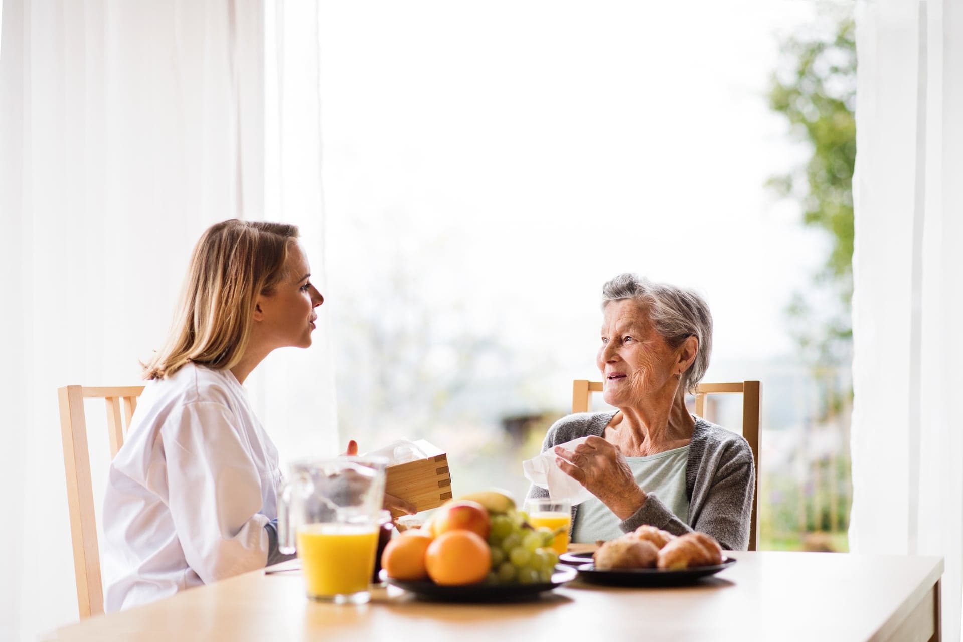 Care worker talking with an older woman at a dining table during a home visit