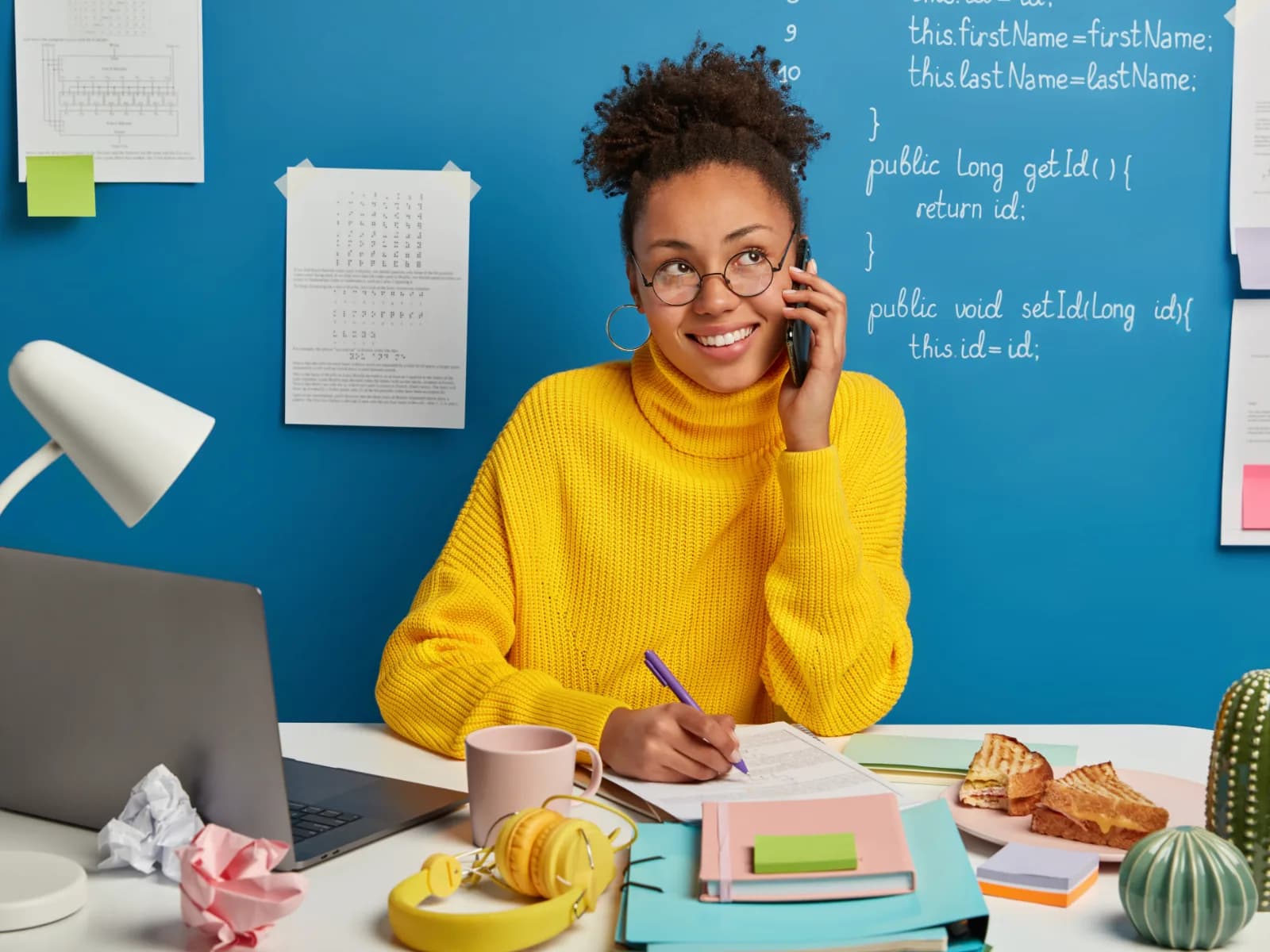 Smiling colleague taking notes during a phone conversation in a colourful workspace.