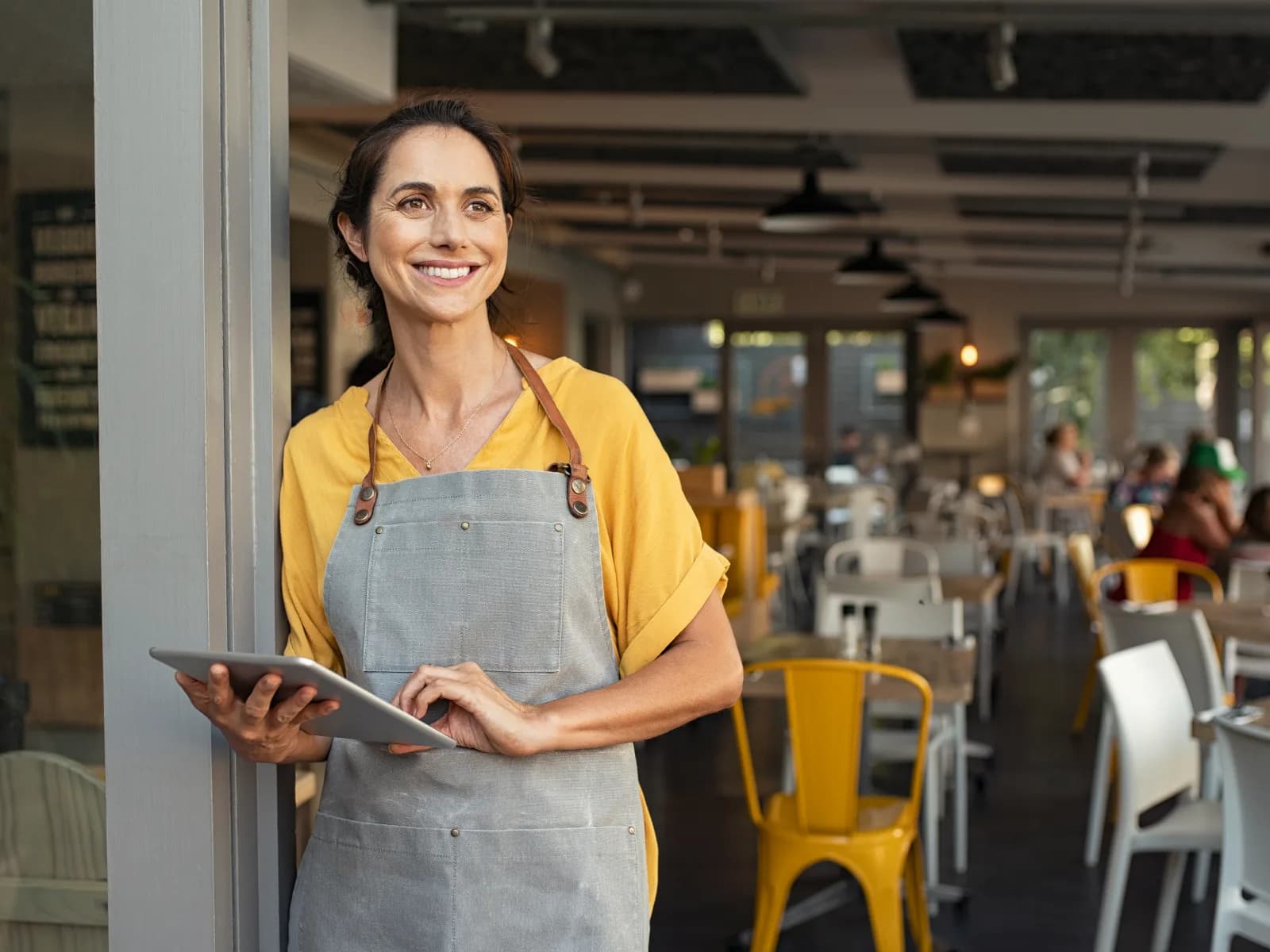 Café owner holding a tablet at the entrance to her workplace.