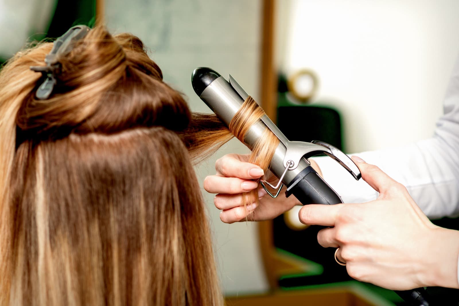Hairdresser curling a client’s brown hair with a curling iron in a salon.